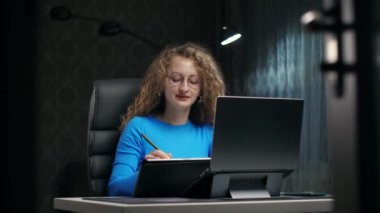 Karanlık odada oturmuş grafik tableti çizen bir kadın. Gözlüklü dijital ressam, Stylus 'la uzaktan yakından evde dizüstü bilgisayara bakıyor. Kıvırcık kız kalemle resim yapmayı öğreniyor. Yüksek