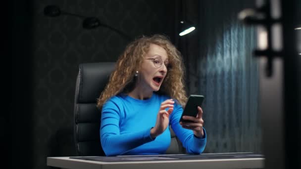 Curly Woman Excited Using Phone Sitting Dark Room Surprised Girl — Wideo stockowe