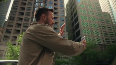 Sakallı genç adam şehrin arka planında akıllı telefon kullanarak görüntülü arama yapıyor. Adam elinde telefonla sosyal medya için iletişim kaydı videosu çekiyor. Cep telefonu kamerasına el sallayan bir erkek. Yüksek