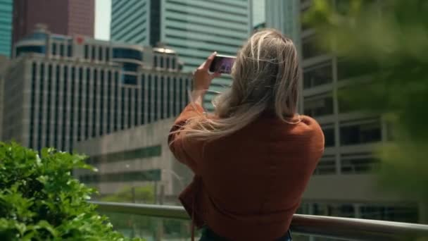 若い金髪の女性が写真を撮る現代都市の建物 セルフィーのための電話を使用して女性 スマートフォンをスクリーンで見ている魅力的な女性 高品質の4K映像 — ストック動画