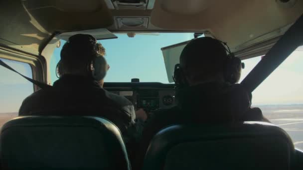 飛行機の飛行機のパイロット2人 飛行機のキャビンに座っているヘッドフォンを着用したヤングビードマンは 曇った日光の背景に飛んでいます 高品質の4K映像 — ストック動画
