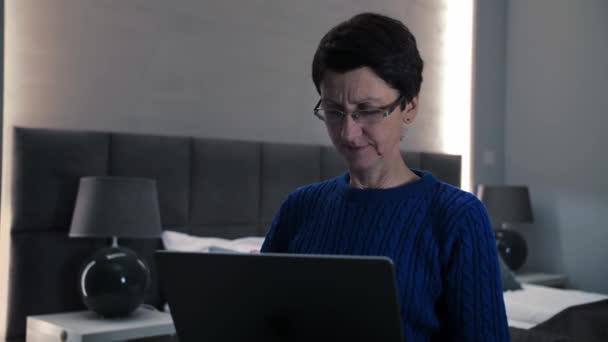 自宅でラップトップを使用して中年女性 大人の女性は ソファに座ってコンピュータがどのように動作するかを把握しようとします インターネットを閲覧する眼鏡を持つ女性は コンピュータを使用します 高品質の4K映像 — ストック動画