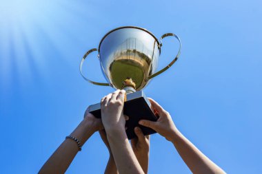 Mavi gökyüzü arkaplanına karşı altın kupa kazanan eller, kazanan başarı konsepti. 