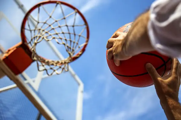 Close-up hands of basketball player aims the ball in the basket against blue sky. Success, scoring, winning and achieving the goal concept