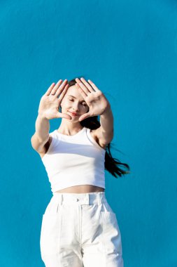 Güzel, genç bir kadın. Uzun koyu saçlı ve elleri mavi arka planda, yüze yakın. Esmer, dur dikey gösteriyor.