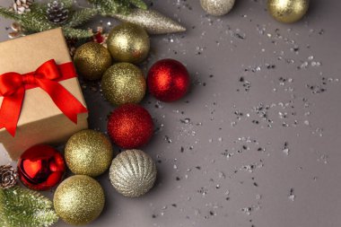 Kırmızı kurdeleli hediye kutusu ve gri arka plan davetiye kartında fotokopi alanı olan renkli Noel süslemeleri.