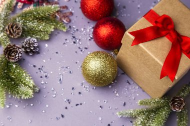 Kırmızı kurdeleli hediye kutusu ve mor arka plan davetiyeli renkli Noel süslemeleri.