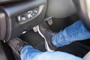 Adamın ayakları siyah spor ayakkabılarla yerde bir arabada fren pedalına basıyor, dikkatle araba sürüyor, trafik ışığı konseptini bekliyor.