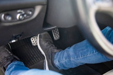 Adamın ayakları siyah spor ayakkabılarla yerde bir arabada fren pedalına basıyor, dikkatle araba sürüyor, trafik ışığı konseptini bekliyor.