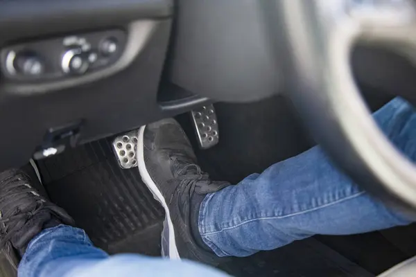 man\'s feet in black sneakers on the floor in a car pushing down the brake pedal, carefully driving car, waiting on the traffic light concept