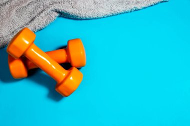 İki dambıl gri havlu ve turkuaz arka planda bir şişe su.