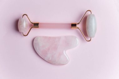 Yüz masajı silindiri ve pembe arka planda gua sha taşı izole edilmiş kopya alanı