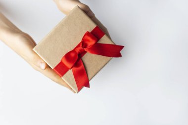 Beyaz arka planda kırmızı kurdeleli hediye paketi tutan eller. 