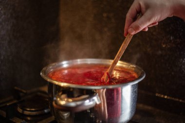 Mutfaktaki bir gaz sobasında, bir tencerede ahşap kaşıkla çorba pişirmek.
