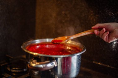 Mutfaktaki bir gaz sobasında, bir tencerede ahşap kaşıkla çorba pişirmek.