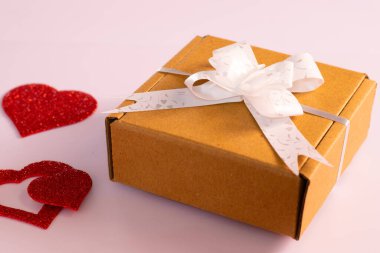 Kırmızı renkli kalp şablonu pembemsi arkaplanlı kırmızı parlayan çarşaftan alınmış. Sevilen kişiye hazırlanmak için yanında beyaz bir çekici ile kahverengi hediye kutusu var.