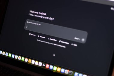Teknisyen Grok 'u cep telefonuyla bilgisayar ekranında denerken Grok logosu gösteriyor. Elon Musk' un üretken, konuşkan, sinirsel bir ağı var.
