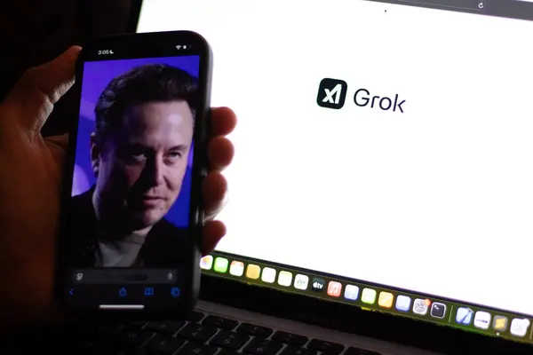 Teknisyen Grok 'u cep telefonuyla bilgisayar ekranında denerken Grok logosu gösteriyor. Elon Musk' un üretken, konuşkan, sinirsel bir ağı var.