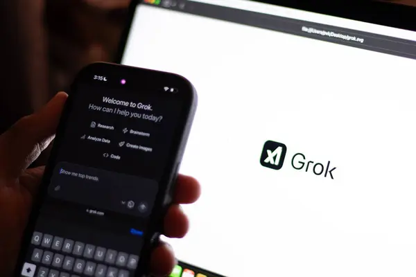 Teknisyen Grok 'u cep telefonuyla bilgisayar ekranında denerken Grok logosu gösteriyor. Elon Musk' un üretken, konuşkan, sinirsel bir ağı var.