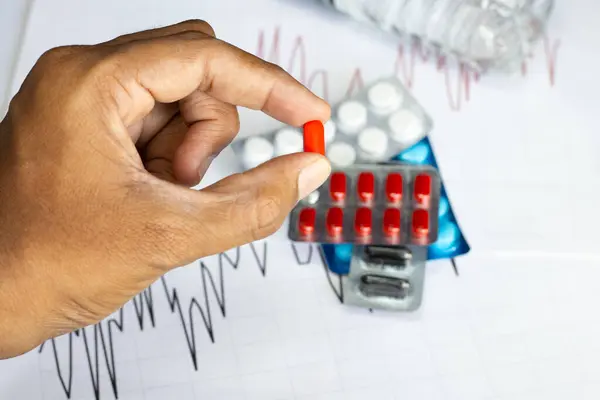 Elinde farklı renklerde haplar tutan adam, ilaç enflasyonunu arka plan çizelgeleri ve hap kılıflarıyla gösteriyor.
