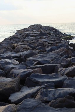 Okyanustaki dalgaların saldırganlığını azaltmak için kıyılar arasında büyük siyah kaya taşları tutulur.