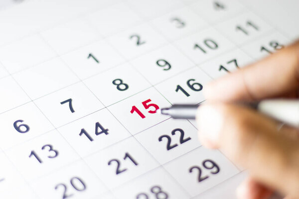 Calendar with number 15 highlighted in red color with hand holding pen to point the number 15