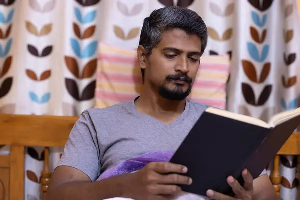 Kitap bağımlılığı, yatakta kitap okuyan bir adam. Fransız sakallı, kitap okuyan Asyalı bir Hintli.