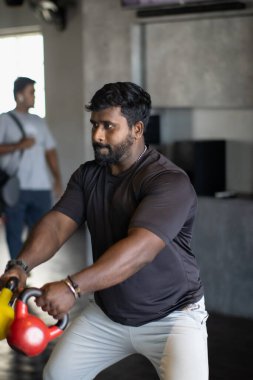 Yakışıklı bir adamın portresi kırmızı ve sarı kettlebell kaldırıyor.