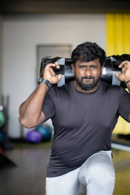 Spor salonunda ağırlık kaldıran Asyalı Hintli bir adamın portresi.