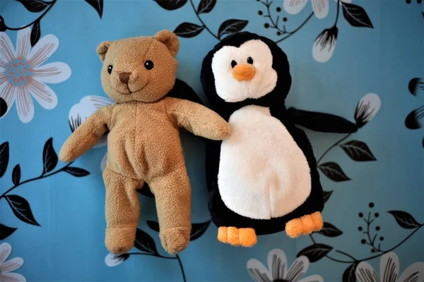 plush toys of a brown bear and a penguin