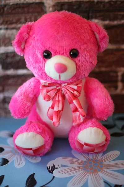 Plush teddy bear in pink color sitting, with white details sitting