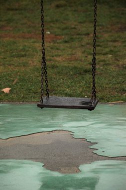 an old wooden swing with chains attached, in a children's playground where no one is