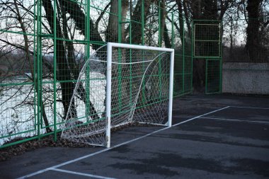 A white goal that has a net on the field behind the green protective fence for indoor soccer located next to the lake