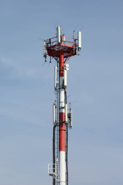 Red and white tower for signaling and communication with a ladder to climb to the top, blue sky