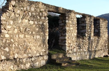Taş ve çamurdan yapılmış eski bir evin kalıntıları, yeşillik ve mavi gökyüzü, güneş ışığı