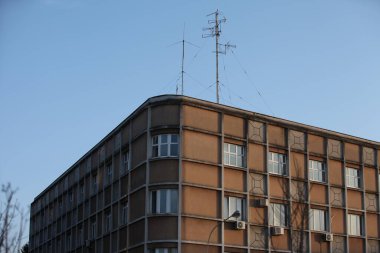 Eski bir apartmanın köşesi, çatıda anten, mavi gökyüzü.