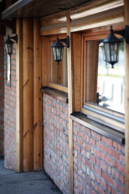Evin önündeki duvara asılı fenerler, tuğla bir duvar ve ahşap pencereler.