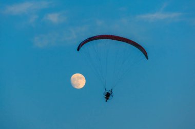 Mavi gökyüzünde dolunay ve hava sporlarıyla paraşütle atlamak