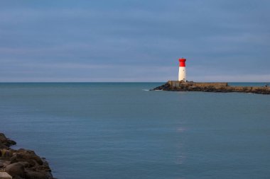 Bir deniz feneri kayalık bir kıyı şeridinde, okyanus dalgaları kayalara çarpıyor. Deniz feneri kırmızı ve beyazdır ve kayalık bir kıyı şeridiyle çevrilidir. Sahne sakin ve huzurlu.