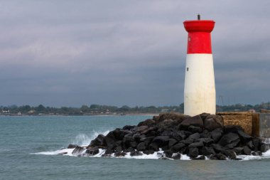 Bir deniz feneri kayalık bir kıyı şeridinde, okyanus dalgaları kayalara çarpıyor. Deniz feneri kırmızı ve beyazdır ve kayalık bir kıyı şeridiyle çevrilidir. Sahne sakin ve huzurlu.