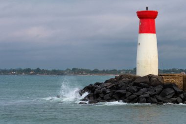 Bir deniz feneri kayalık bir kıyı şeridinde, okyanus dalgaları kayalara çarpıyor. Deniz feneri kırmızı ve beyazdır ve kayalık bir kıyı şeridiyle çevrilidir. Sahne sakin ve huzurlu.