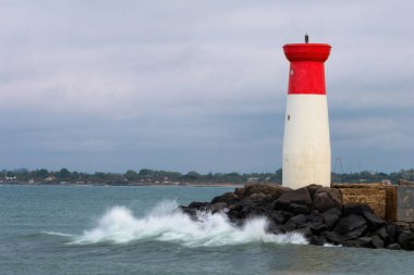 Bir deniz feneri kayalık bir kıyı şeridinde, okyanus dalgaları kayalara çarpıyor. Deniz feneri kırmızı ve beyazdır ve kayalık bir kıyı şeridiyle çevrilidir. Sahne sakin ve huzurlu.