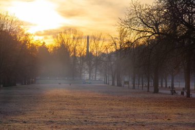 Islak ve delikli bir yolu olan bir park. Güneş batıyor ve gökyüzü turuncu.