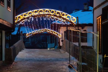 A bridge lit up with lights and a fence in the background, Tryavna. Scene is festive and warm clipart