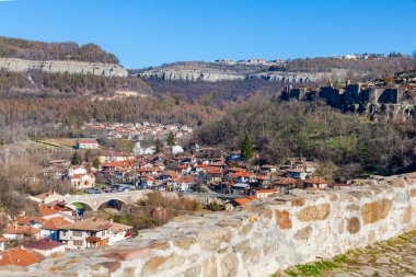 Arka planda bulutlu bir gökyüzü olan tepedeki Çarevets Kalesi. Kale ağaçlar ve kayalarla çevrili.