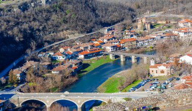 Arka planda bulutlu bir gökyüzü olan tepedeki Çarevets Kalesi. Kale ağaçlar ve kayalarla çevrili.