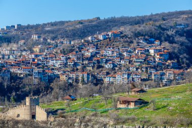 Arka planda bulutlu bir gökyüzü olan tepedeki Çarevets Kalesi. Kale ağaçlar ve kayalarla çevrili.