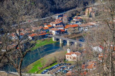 Arka planda bulutlu bir gökyüzü olan tepedeki Çarevets Kalesi. Kale ağaçlar ve kayalarla çevrili.