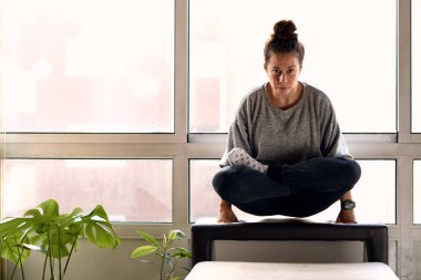 Woman meditating in a couch indoors surrounded by plants