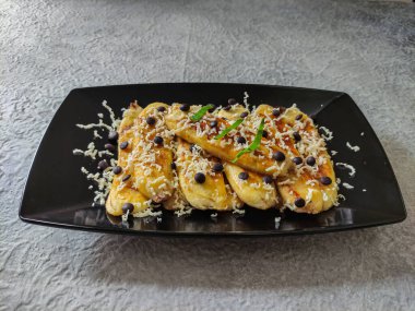 Izgara muz, rendelenmiş peynir ve çikolata parçacıkları. Gri desenli arka planda siyah tabakta servis edilmiş. Seçici odak resmi.